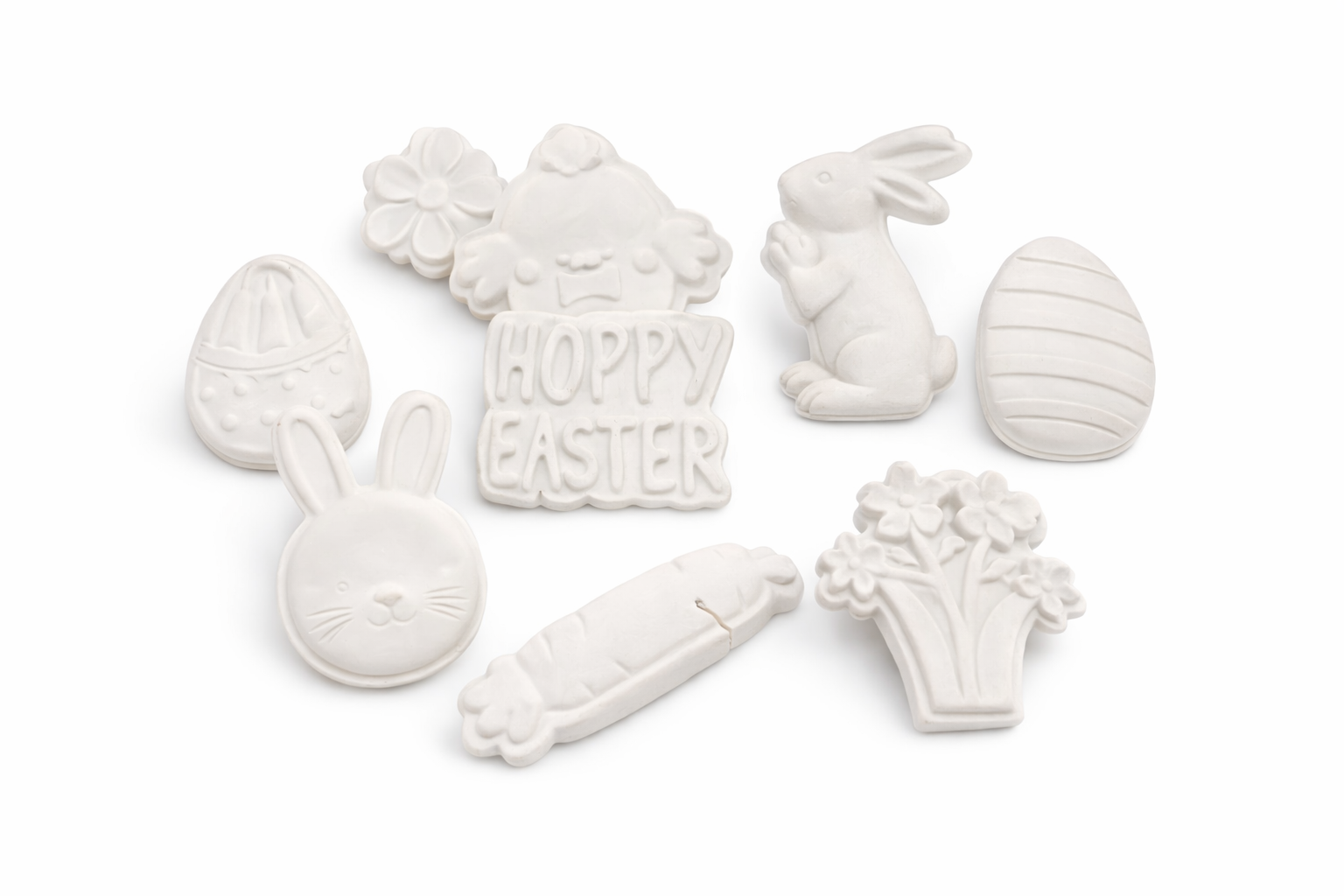 White plaster Easter molds including decorated eggs, bunny rabbits, Hoppy Easter sign, flowers, and carrot shapes arranged on white background